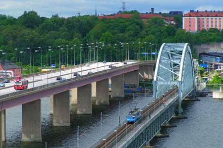 Alla som ska ta sig till Lidingö på hjul, med bil, buss, tåg, cykel eller genom att gå, måste göra det på någon av de två Lidingöbroarna. Den stora, till vänster, invigdes 1971 och den låga "Gamla Lidingöbron" till höger, invigdes 1925 men är nu helt ersatt av "Lilla Lidingöbron". Längst till höger skymtar Ropstens tunnelbanestation och i bakgrunden syns Hjorthagen i Stockholm. Den nya "Lilla Lidingöbron", som ersatt Gamla Lidingöbron, skulle vara helt klar i september 2023 men det dröjde till slutet av maj 2024 innan Lidingöbanan började köras över bron. Den gamla bron med sin nästan 100 år gamla, välkända båge, är nu helt riven. Men denna bild får vara kvar.